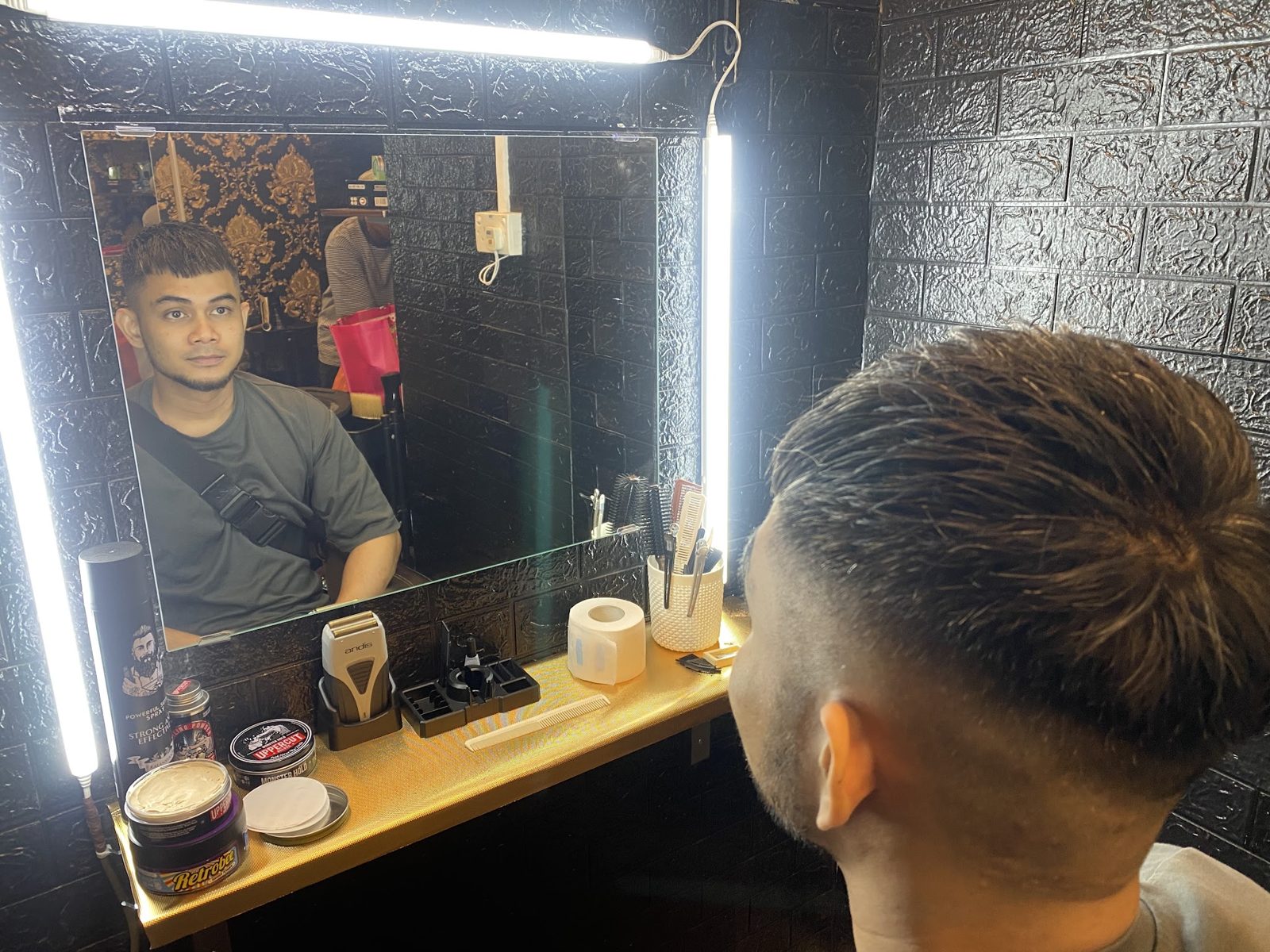 A barber at a mirror under LED strip lighting
